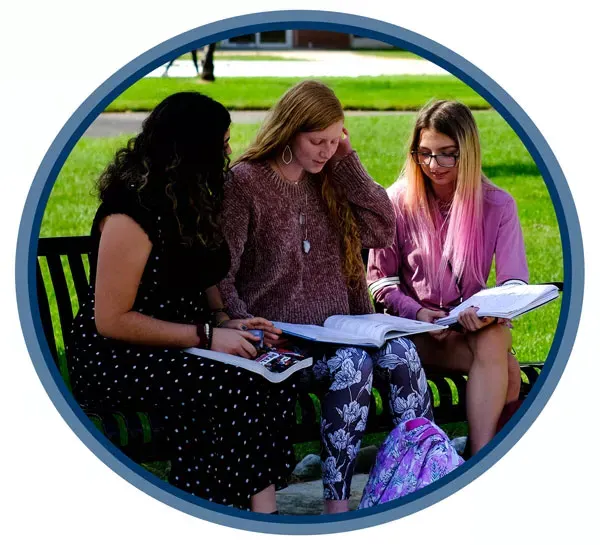 three students sitting on a bench on campus studying